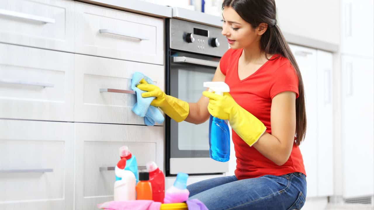 woman in protective gloves cleaning kitchen cabinet