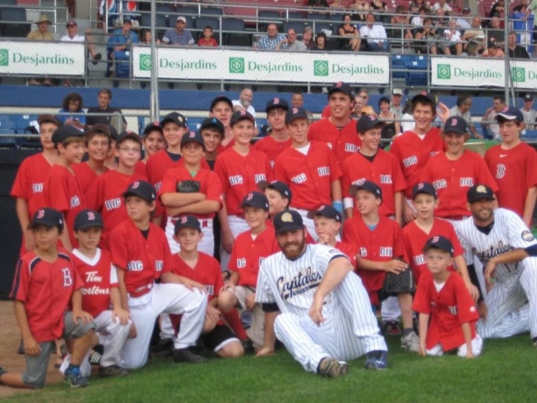 A group of kids in baseball uniforms take a group photo on the field