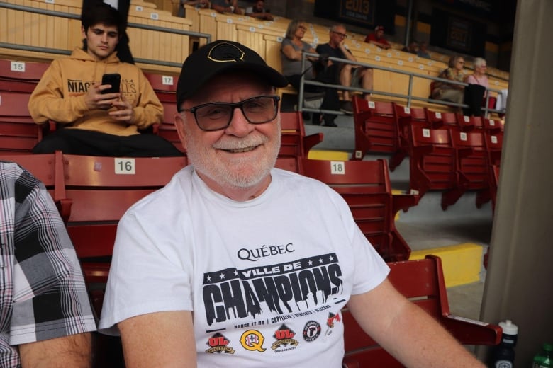 A man smiles at the camera. He is sitting in a stadium.