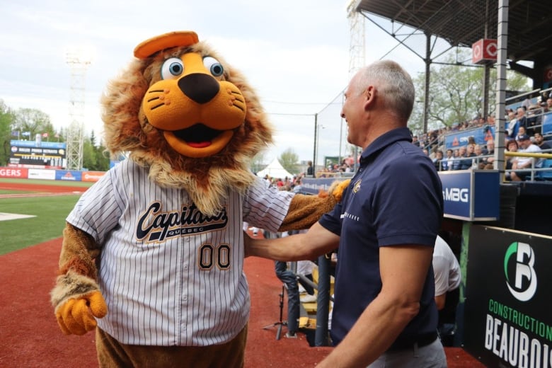 A mascot wearing a baseball jersey interacts with a man on the baseball field