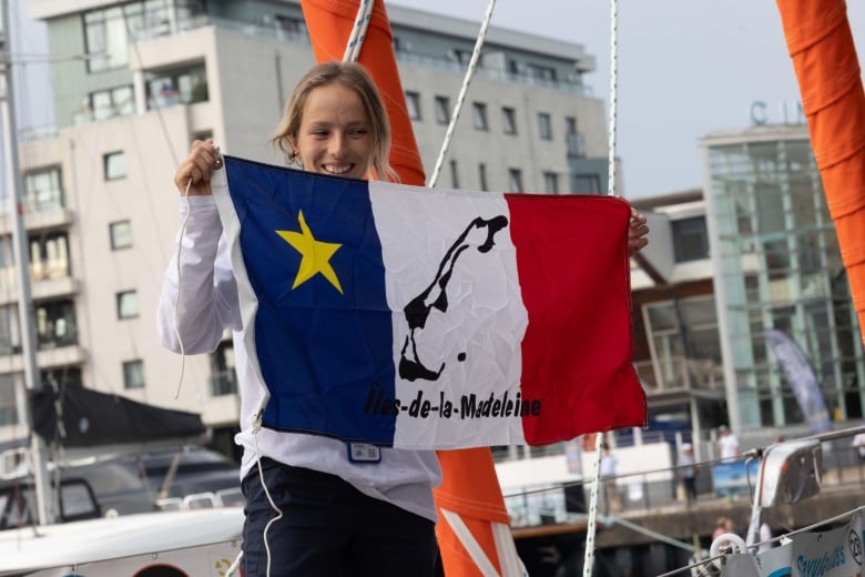 A woman stands on a sailboat holding a flag of Quebec's Magdaleine Islands 