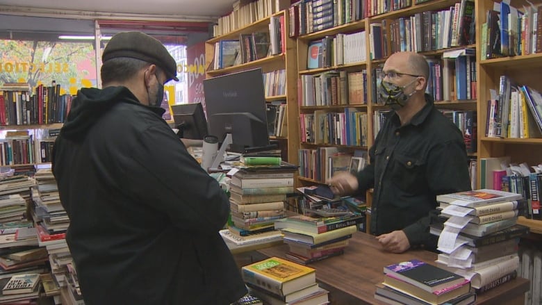 A man stands behind a counter covered in books, helping a customer purchase books.