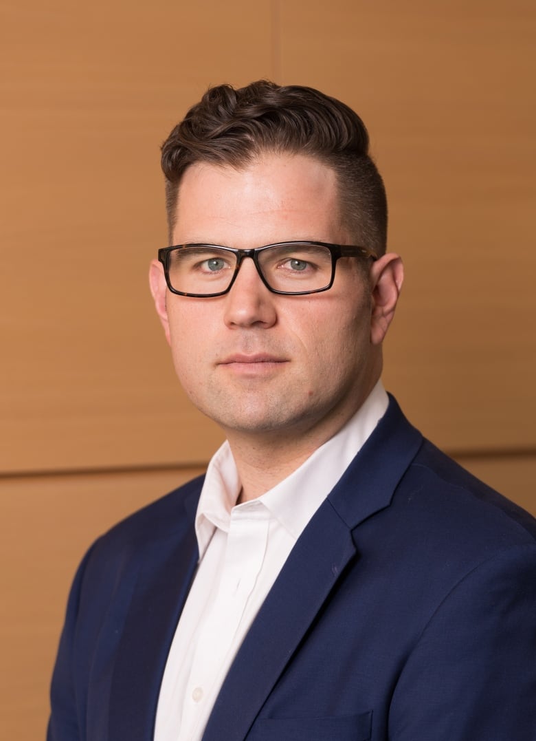 Darren Brenner wears glasses and a navy suit jacket in this photo.