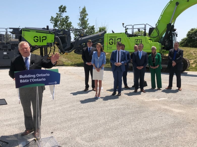 Ontario Premier Doug Ford stands at a podium with a crowd of people behind him to the right. 