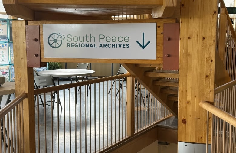 Wooden staircase. The sign that hangs off the staircase reads "South Peace Regional Archives." The arrow on the sign is pointing down. 