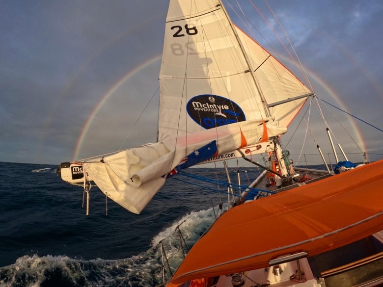 A sailboat on the ocean in the background is a double rainbow. 