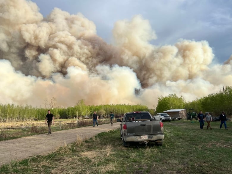 Sky of smoke, people walking on dirt road, pickup truck.