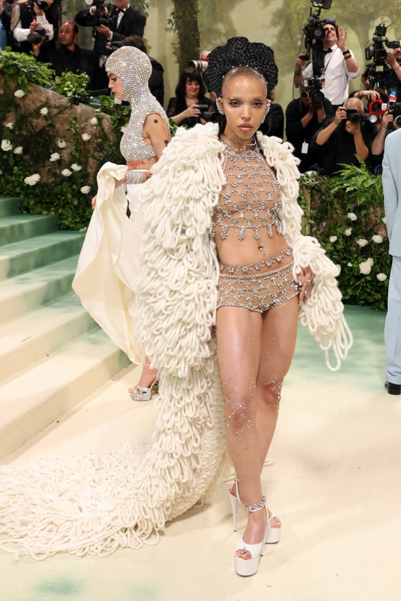 FKA twigs on the Met Gala red carpet wearing a cream cape with loops and a 2-piece diamond-embellished top and bottoms. 