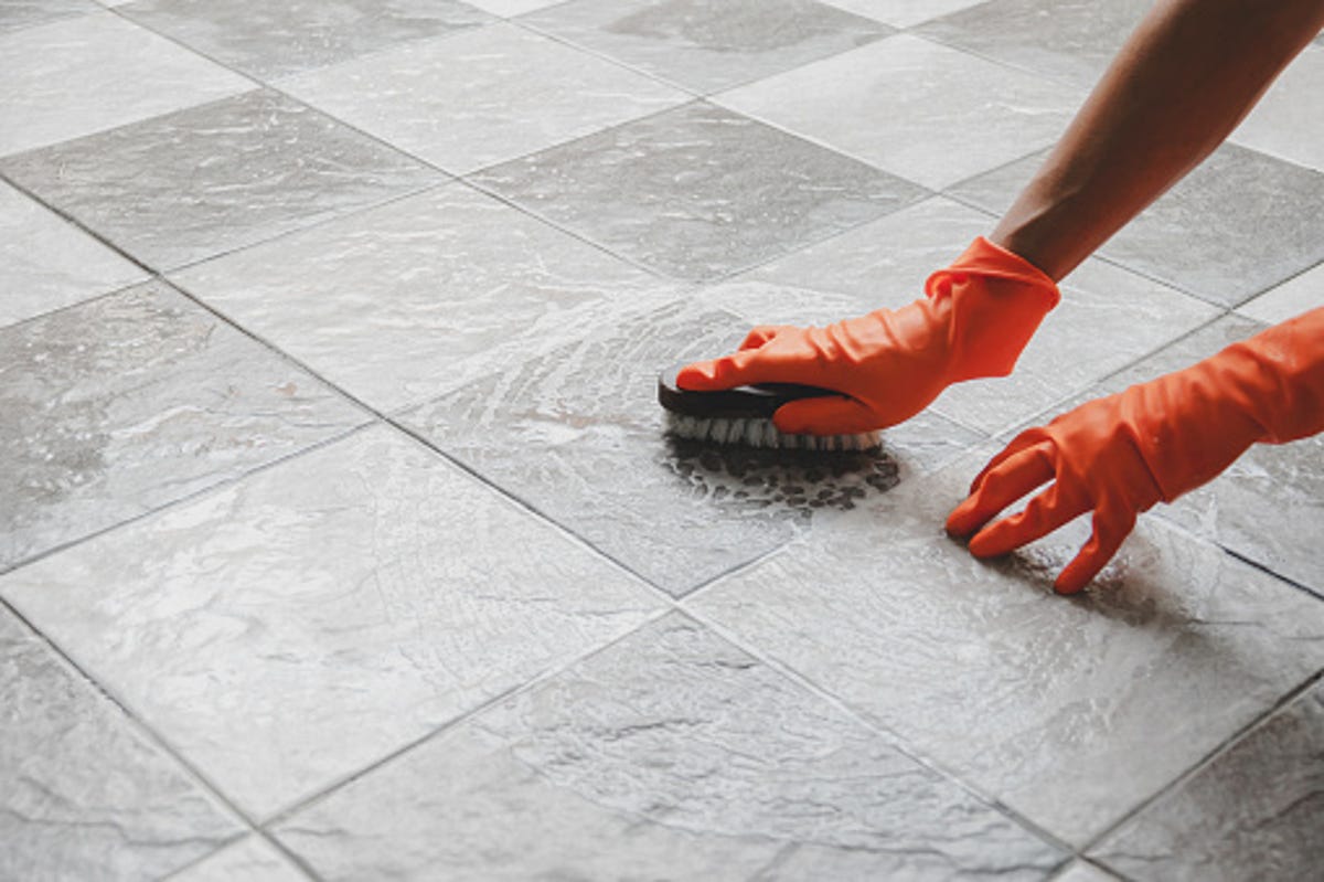 Person with orange gloves scrubbing a tile floor