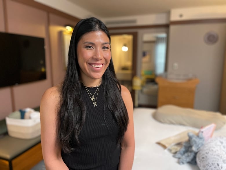 A woman with long black hair wearing a black tank top is pictured standing inside a Toronto hotel room.