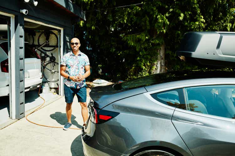 Smiling father standing behind electric car before beginning family road trip