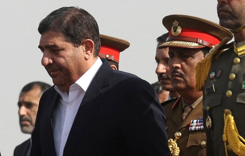 A government official on the left walks with a military guard.