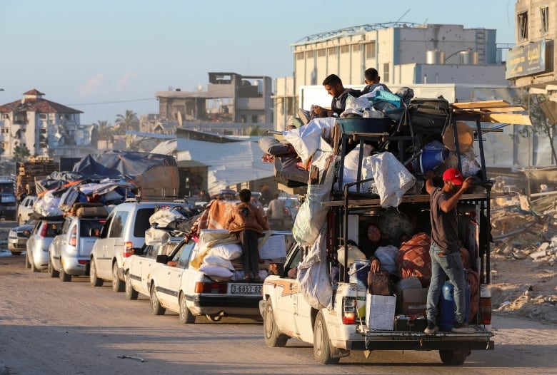 A convoy of cars laden with belongings and people drives on an urban road. 