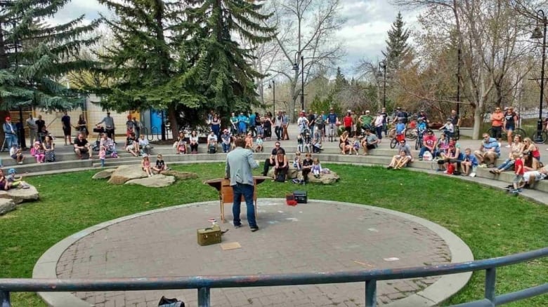 A man performs in an outdoor setting with a crowd looking on.