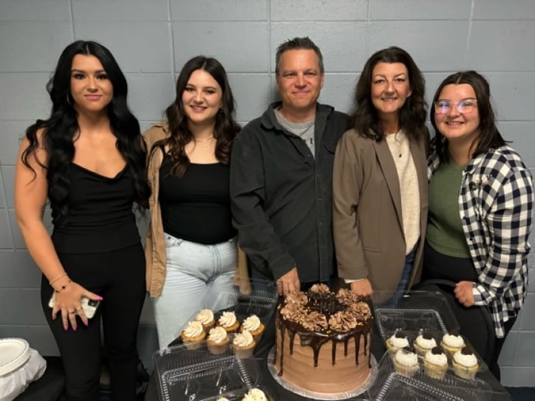 A family of four women and one man pose in front of baked goods.