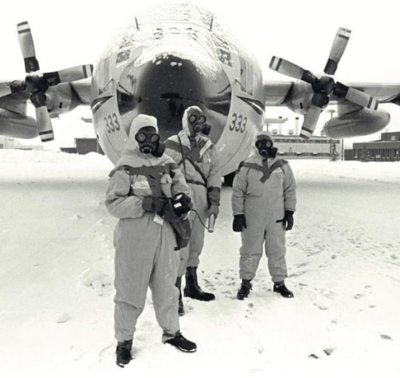 Three members of the Operation Morning Light team stand in front of an airplane in uniform, wearing gas masks.