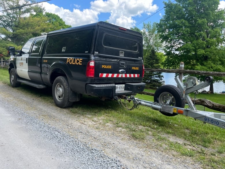 A black-and-white police truck with some sort of trailer attached to the back is parked in front of a lake on a sunny day.