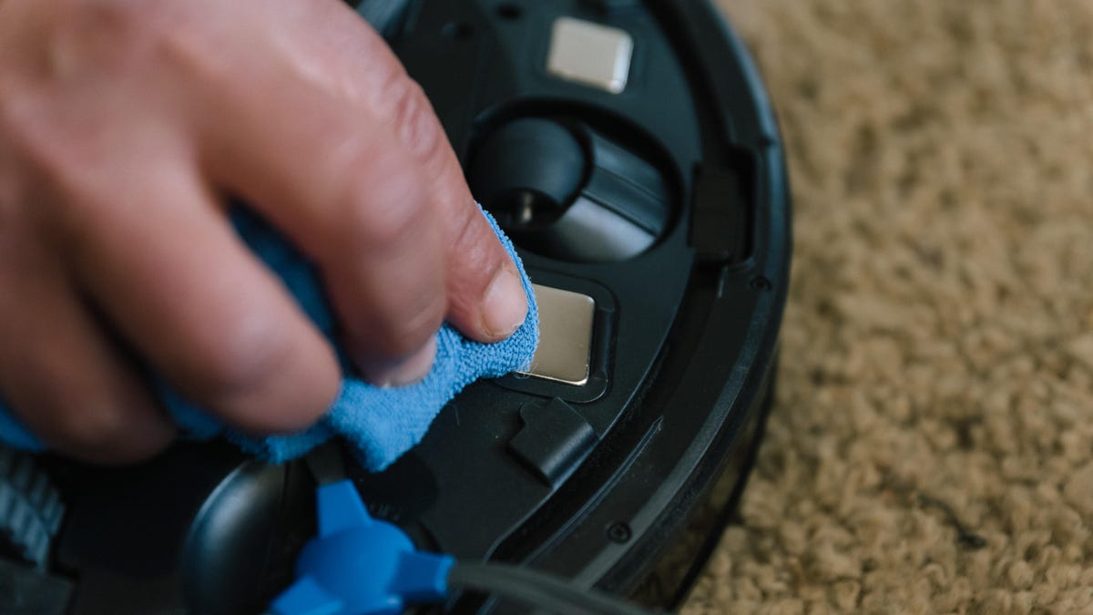 hand wiping down a robot vacuum 