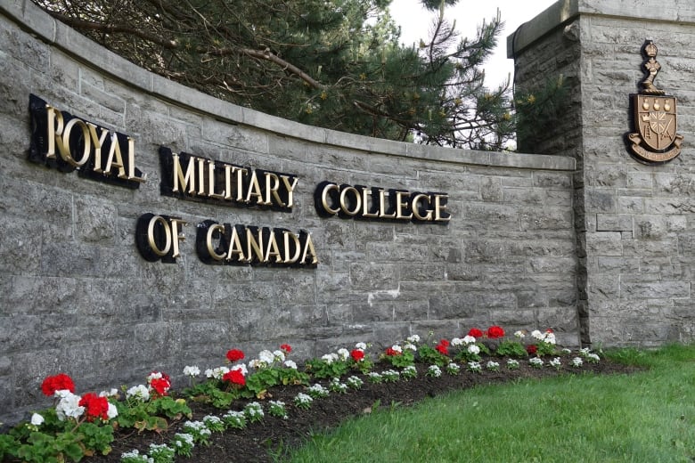 A brick wall with the words "Royal Military College of Canada" in gold letters, with red and white flowers in a bed running in front of it.