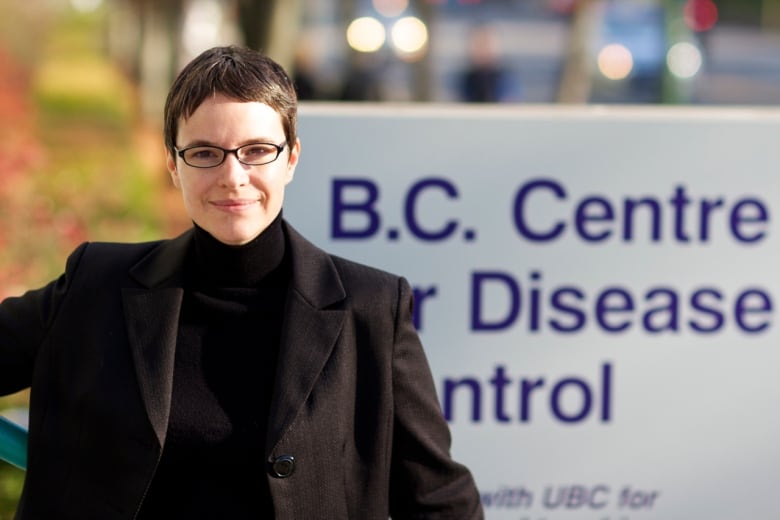 A woman stands in front of a sign for the B.C. Centre for Disease Control in a suit.