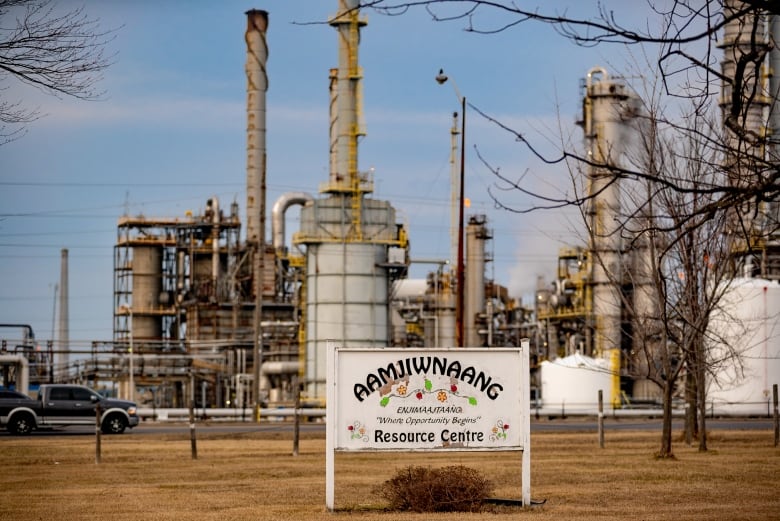 Chemical plants in the background of a sign that reads "Aamjiwnaang First Nation Resource Centre."