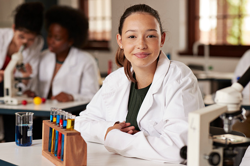 Smiling teenage female student sitting with test tube rack