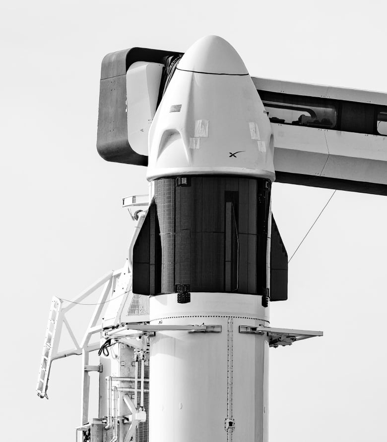 A white rocket with a black and white module sit on a launch pad on a cloudy day.