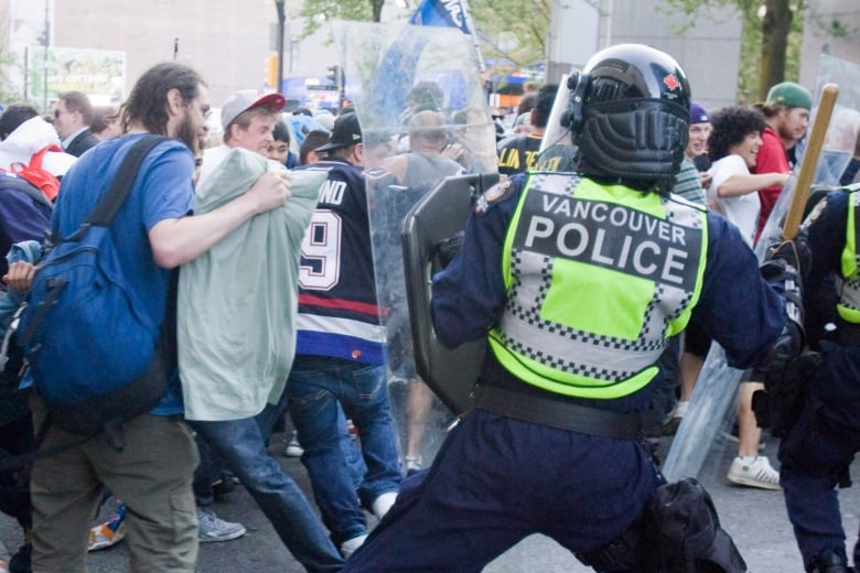 A police officer pushes people back with a shield