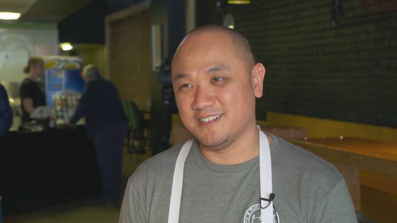 A man wearing a white and brown apron stands in a burger restaurant.