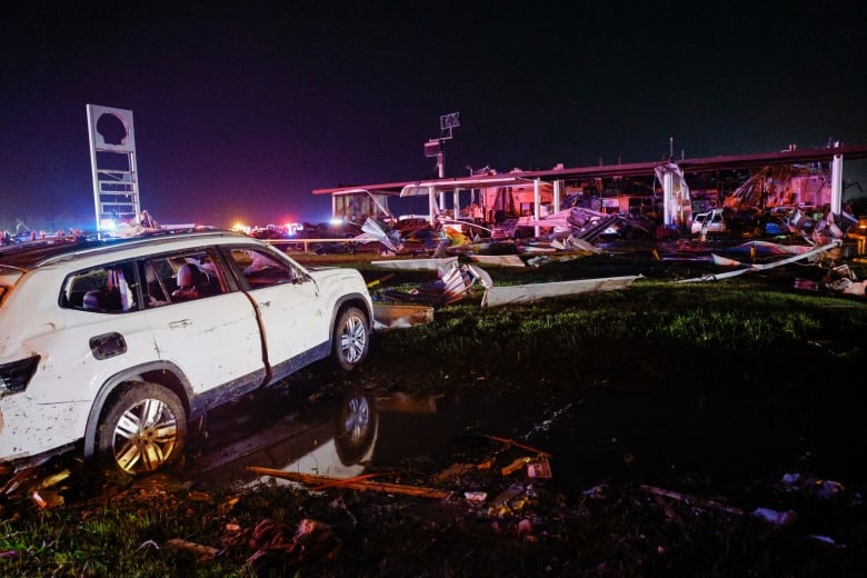 A car rests in a watery ditch near a Shell gas station after a tornado strike.