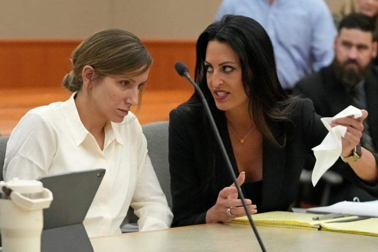 A woman in white sits in a  court beside a woman in a  suit