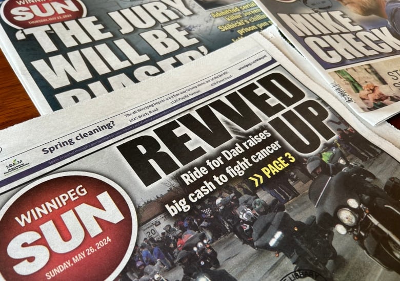 Three front page covers of the Winnipeg Sun newspaper, laid out on a wooden table.