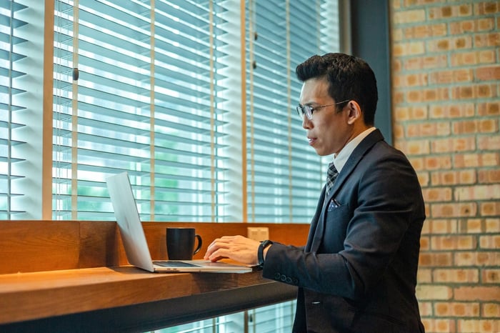 A person in a suit is standing up while typing on a laptop computer.