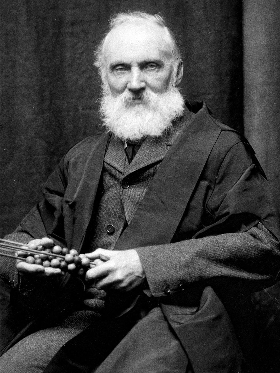 Old photo of an elderly man with a white beard, holding a model of a molecule.