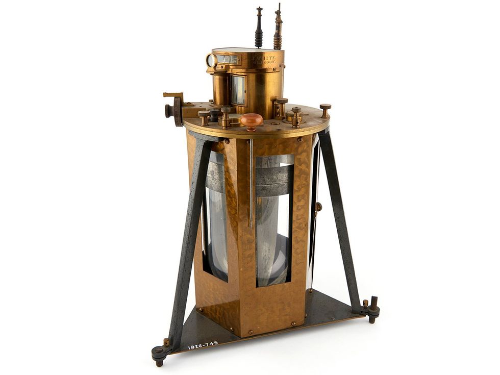 Photo of a brass scientific instrument with a triangular base supporting a 6-sided cylinder.