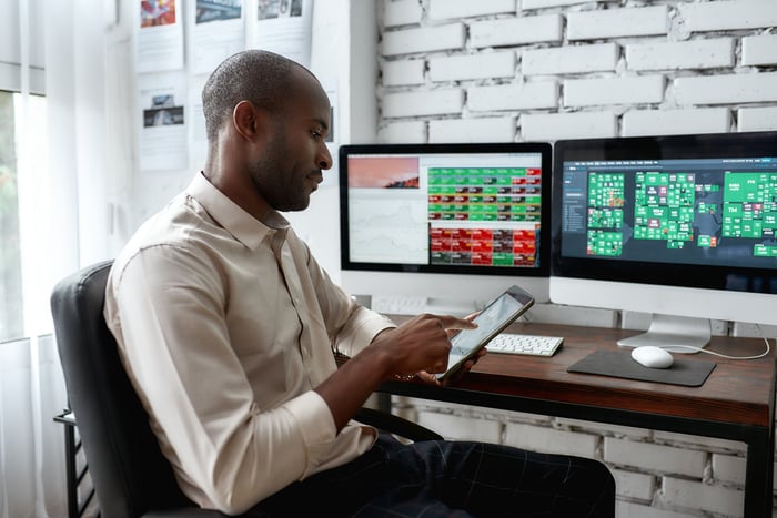 An individual looking at a tablet while two monitors facing them. 