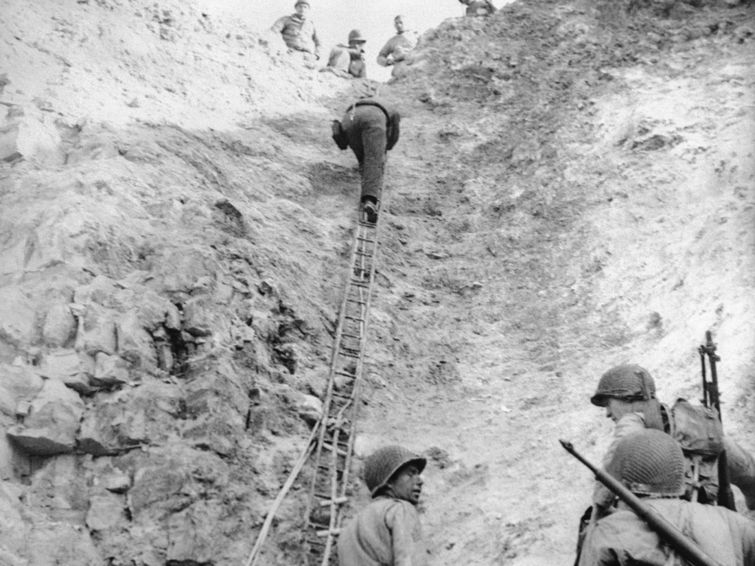 Army Rangers demonstrate climbing up the cliffside on a ladder. 