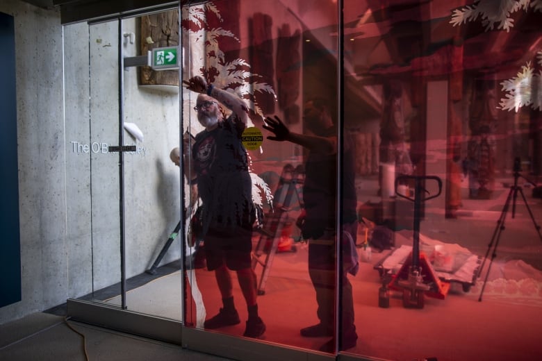 Two men work on a glass wall that is stained with red in a museum.