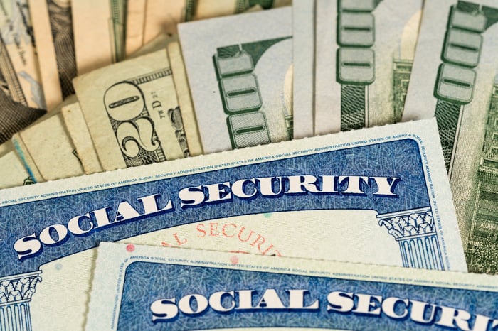 Two Social Security cards lying atop U.S. currency.