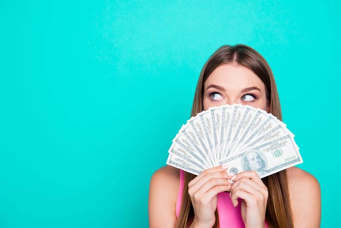 A person hides their face behind a fan of cash.