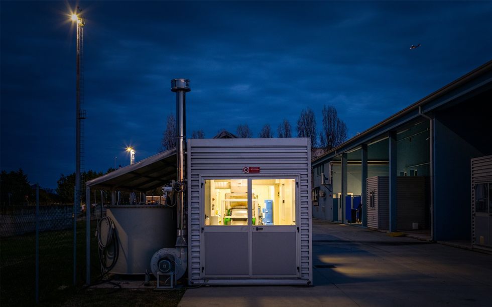 A shipping container lit up from the inside sits in an industrial area at night