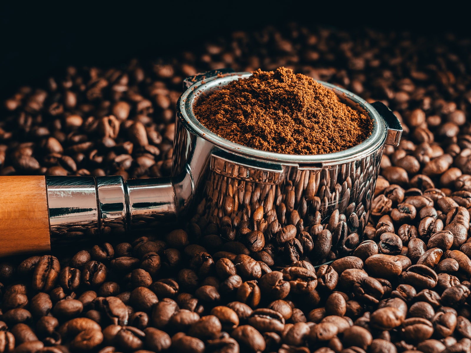 Closeup of a pile of coffee beans with ground beans in a holder on top