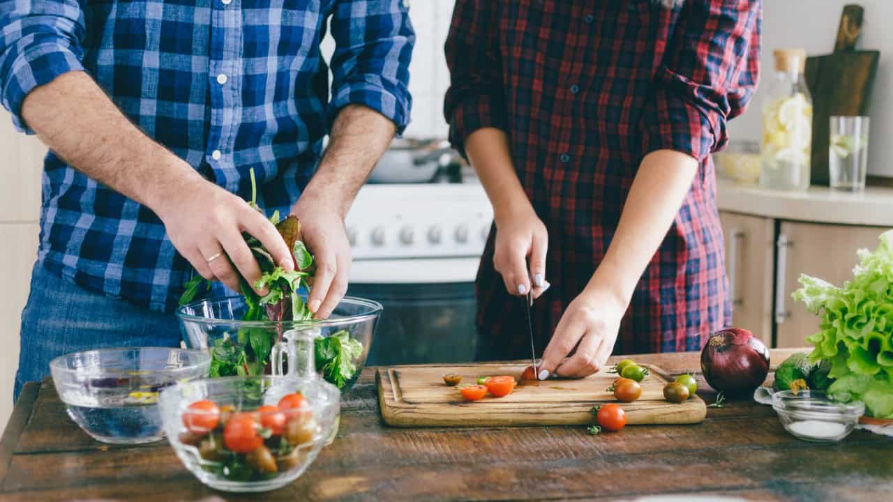 Couple cooking salad with vegetables on wooden table in home kitchen