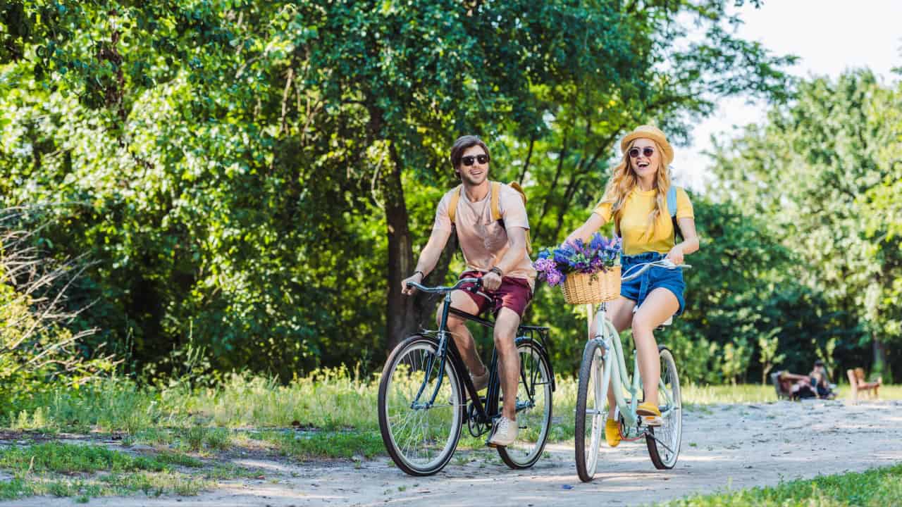 Young happy couple riding retro bicycles in park on summer day