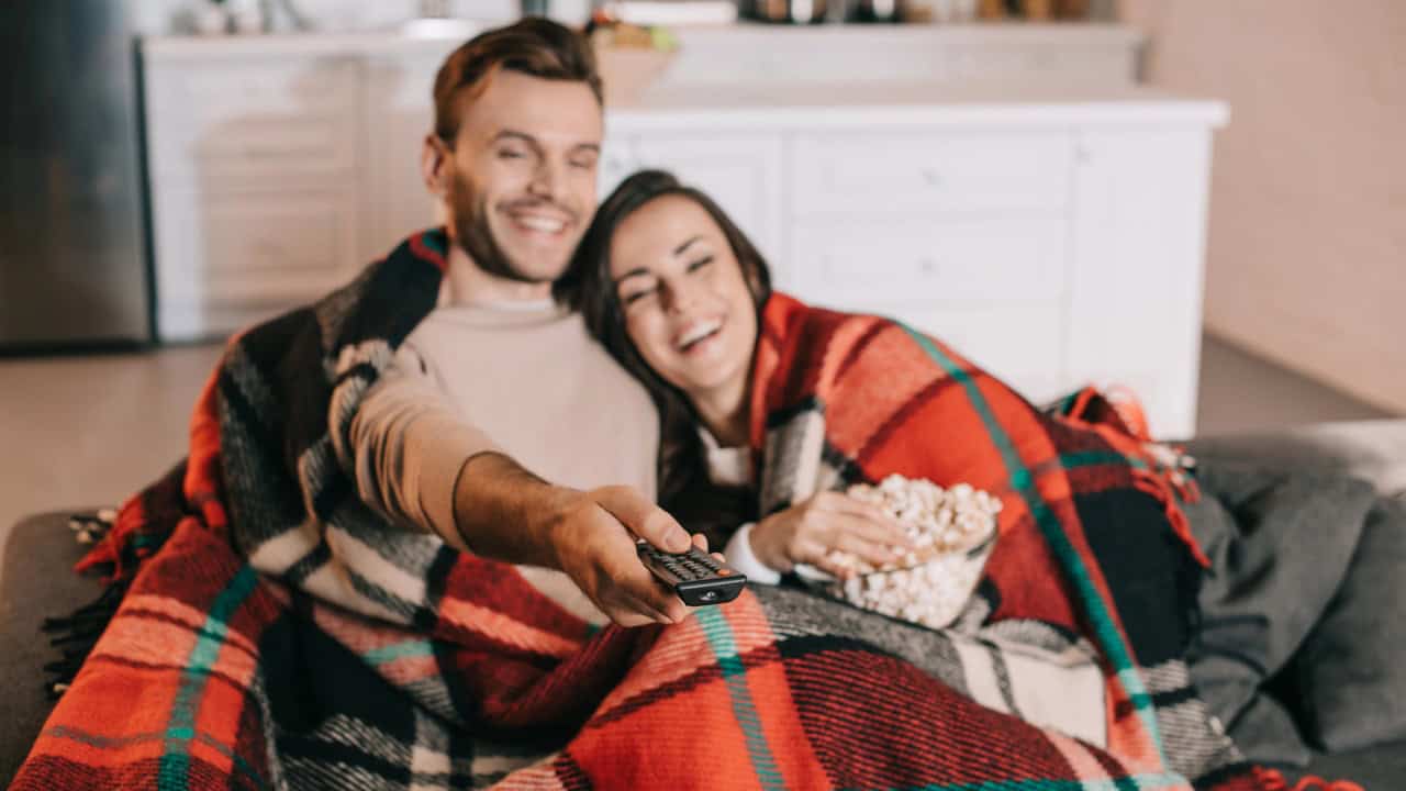 Happy young couple watching tv with popcorn