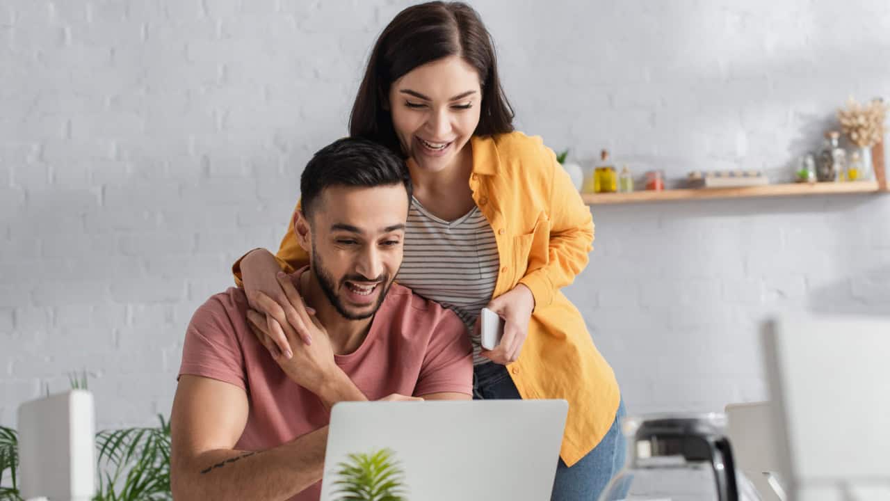 Smiling young woman holding cellphone and touching hands with boyfriend