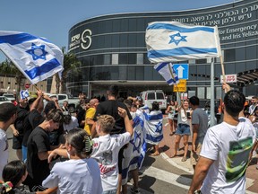 People gather with Israeli national flags outside Sheba Tel-HaShomer Medical Centre in Ramat Gan on Saturday, June 8, 2024 where Israeli hostages were transferred after being freed from captivity in the Gaza Strip since the Oct. 7 attacks, amid the ongoing conflict in the Palestinian territory between Israel and the militant group Hamas.