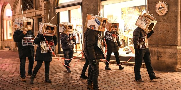 Menschen demonstrieren, sie tragen Pappkartons auf ihren Köpfen, die aussehehn wie altmodische Fernseher