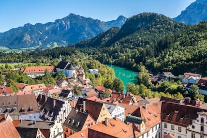 Blick auf die Altstadt von Füssen mit der Pfarrkirche St. Stephan, dem Fluss Lech und den Bergen.