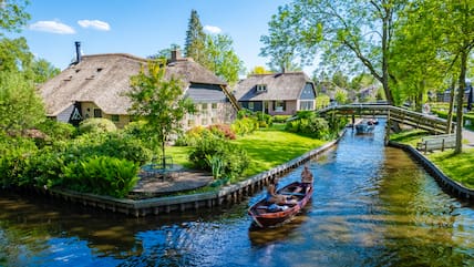 Giethoorn Niederlande: Touristen in Booten besuchen das berühmte Dorf mit Grachten und rustikalen Reetdachhäusern in einem Bauernhofgebiet an einem heißen Frühlingstag